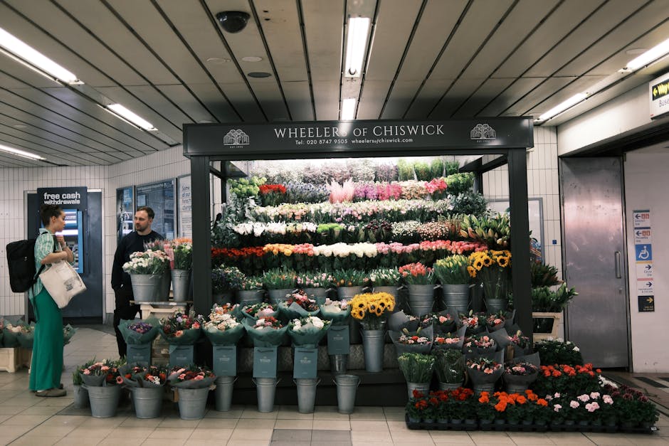 A vibrant floral display at Wheeler of Chiswick within an underground station, featuring a variety of fresh flowers including pink, white, yellow, and orange blossoms arranged in metal buckets and on 