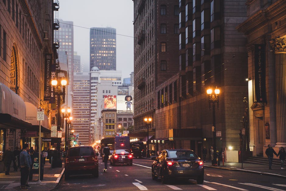 The provided image depicts a city street scene during dusk in South Kensington with tall, historic brick buildings on either side. Street lamps cast a warm glow along the sidewalk, illuminating pedest