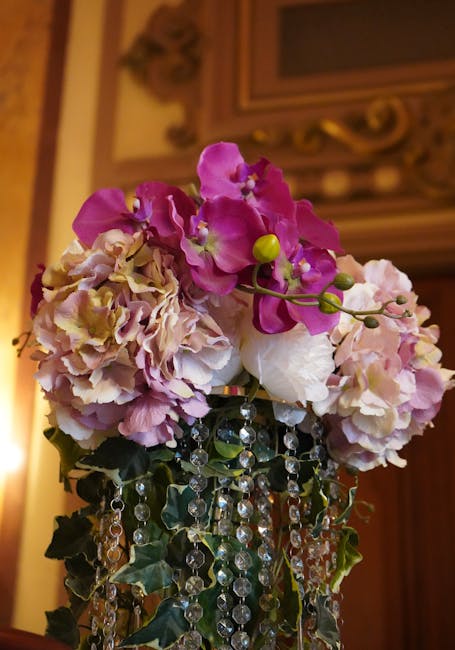 A floral arrangement featuring a cluster of pink and cream hydrangeas with delicate ruffled petals and a few bright pink orchids with smooth, slightly ruffled petals on slender stems, complemented by 